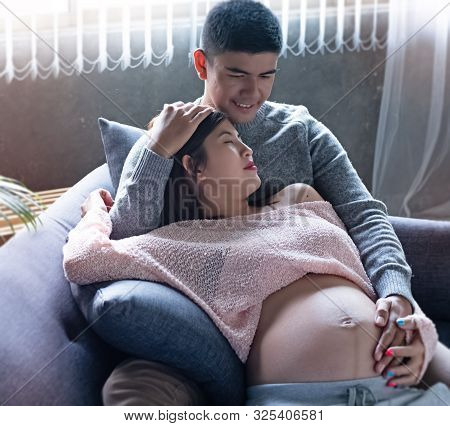 The Pregnant Woman Laying Down On Sofa And Hugging By Her Husband,put Hand Touch Belly,waith For New