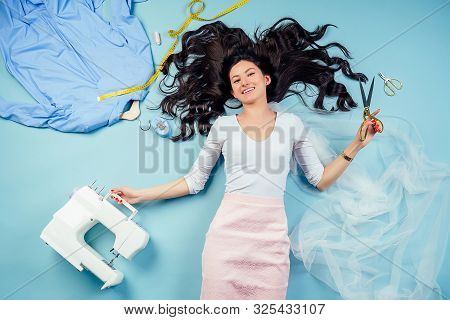 Brunette Woman Seamstress Tailor Dressmaker Lying Fly On The Floor With Sewing Machine, Coats On A H