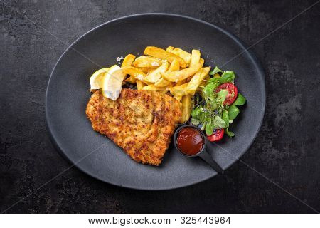 Deep fried Wiener schnitzel from veal topside with French fries and lettuce as top view on a modern design plate 