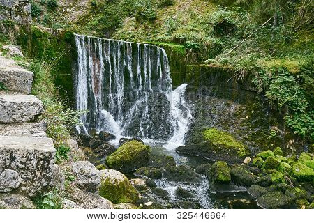 Waterfall At Source Du Doubs Mouthe Franche Comté France With Green Plants On A Sunny Day