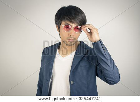 Portrait Asian Casual Businessman In Navy Blue Suit Touching Red Eyeglasses On Grey Background. Casu