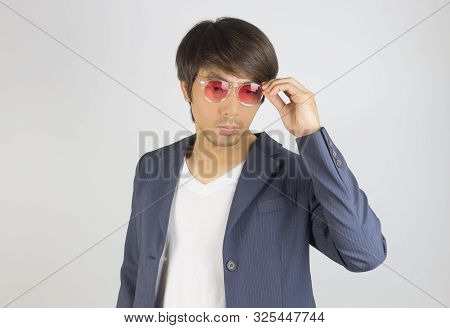Portrait Asian Casual Businessman In Navy Blue Suit Touching Red Eyeglasses On Grey Background. Casu