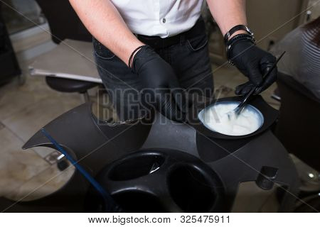 Male Stylist In Gloves Preparing Color Cream For Dying Hairin  A Container, A Mask For Treatment Pro