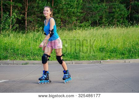 Attractive Young Athletic Slim Brunette Woman In Pink Shorts And Blue Top With Protection Elbow Pads