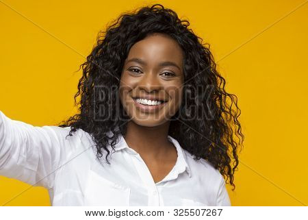 I Love Selfie. Young Afro Woman Holding Cellphone And Making Selfie And Smiling, Yellow Background