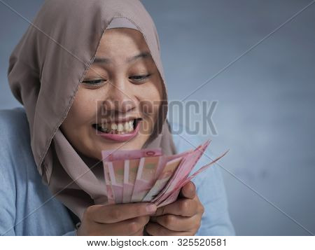 Portrait Of Indonesian Muslim Woman Holding Rupiah Money, Smiling Laughing Winning Gesture