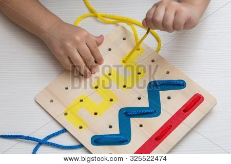 Child Plays Educational Game Interestedly With Wooden Colorful Board And Laces. Development, Educati