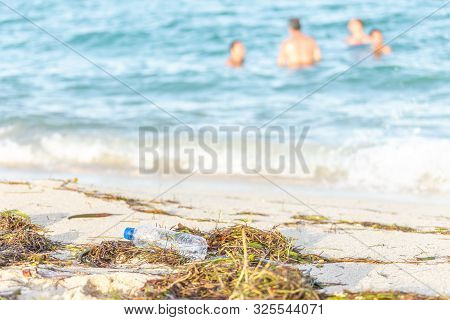 Close Up Image Of Empty Plastic Water Bottle On Dirty Beach Filled With Seaweed, Garbage And Waste O