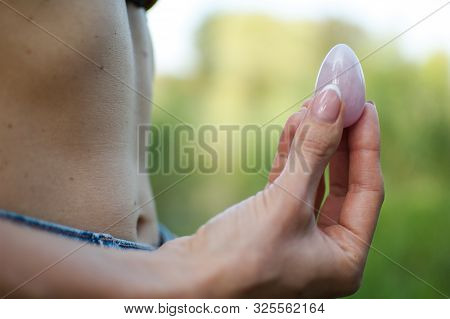 Side View Of Adult Woman Holding Pink Quartz Yoni Egg For Vumfit, Imbuilding Or Meditation Outdoors 
