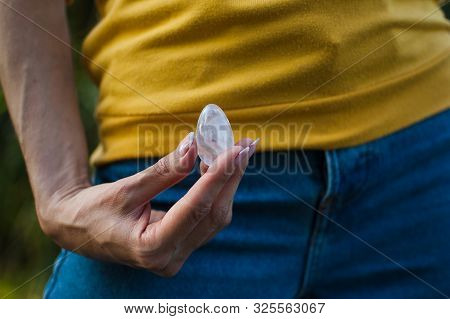 Adult Girl In Yellow Shirt And Blue Jeans Is Holding Transparent Violet Amethyst Yoni Egg For Vumfit