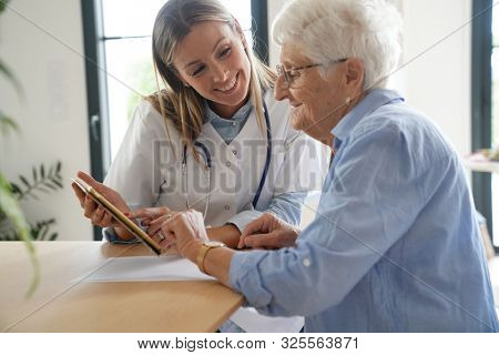 Elderly woman with nurse at home looking at tablet