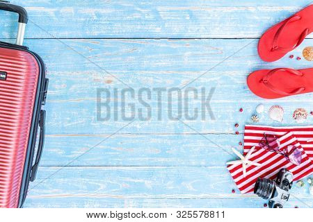 Red Summer background with camera starfish sandle sunglasses and luggage on blue wooden table background with copy space