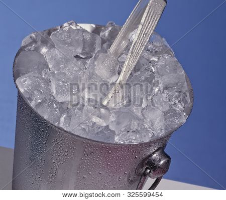 Shot Of A Bucket Of Ice With Tongs And A Blue Background