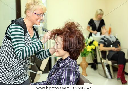 Sorridente parrucchiere rende i capelli styling per donna di rake-pettine nel salone di bellezza; concentrarsi sul client; Othe