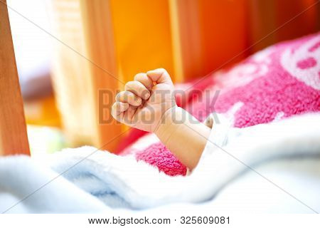 Hand Of An Energetic Newborn Baby With Light Blue And Pink Blanket And Baby Bed. Close Up.