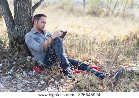 Man Reads An Old Book Propped Up By A Tree. Reading A Book In Nature. Man Reading, Sit Down, Propped