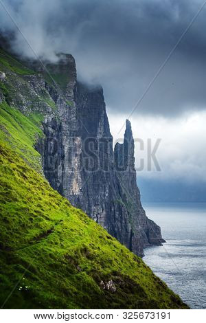 Gorgeous faroese landscape with famous Witches Finger cliffs and dramatic cloudy sky from Trollkonufingur viewpoint. Vagar island, Faroe Islands, Denmark.