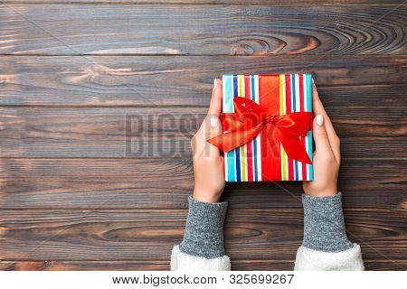 Top View Woman Hands Holding Present Box With Colored Bow On Dark Wooden Background With Copy Space