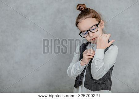 Little Business Lady On A Gray Background. Close-up Dressed In Glasses He Adjusts His Shirt On His S