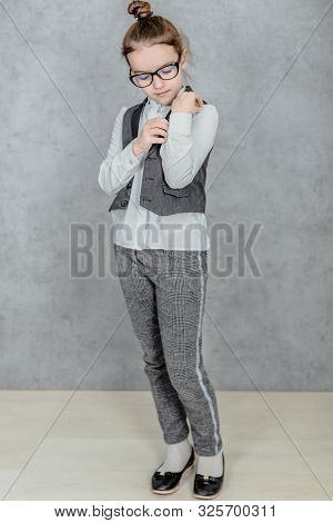 Little Business Lady On A Gray Background. Full Height. Dressed In Glasses He Adjusts His Shirt On H