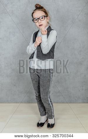 Little Business Lady On A Gray Background. Full Height. Dressed In Glasses He Adjusts His Shirt On H