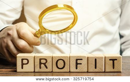 Businessman Holds A Magnifying Glass Over The Word Profit. The Concept Of Profitability And Performa