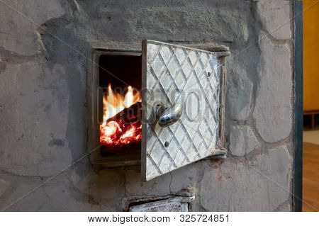 Rustic Stone Stove. The Oven Door Is Open. A Fire Burns In The Firebox. Background.
