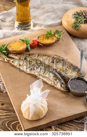 Fried Smelt Fish, Lemon Slice And Potato Wedges On Paper And Glass Of Beer On Wooden Table Side View