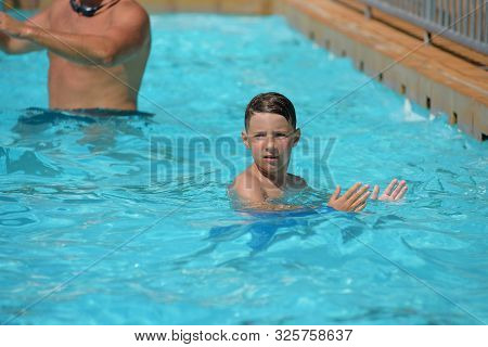 Smiling Caucasian Boy Having Fun In Swimming Pool At Resort. He Dancing Aqua Zumba And Claping Hands