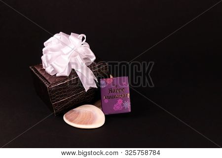 Decorated Brown Lether Box With Happy Anniversary Mini Message Book And Seashell On Black Background