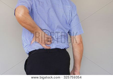 Close-up Elderly Man With Pain In Kidneys Isolated On A Gray Background. Old Man With Back Ache Clas