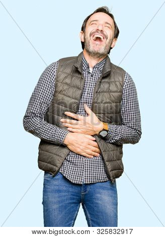 Middle age handsome man wearing winter vest Smiling and laughing hard out loud because funny crazy joke. Happy expression.