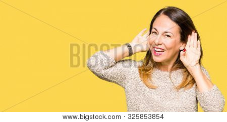 Beautiful middle age woman wearing fashion sweater Trying to hear both hands on ear gesture, curious for gossip. Hearing problem, deaf