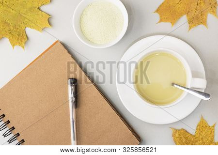 Top View Of Green Tea Matcha In A White Mug,near Notebook For Notes On A Gray Background With Maple 