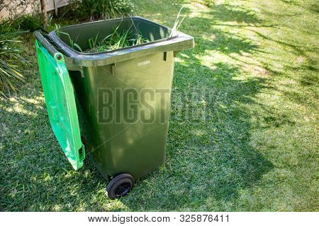 Green Bin Container Filled With Garden Waste. Dirty Gardening Gloves. Spring Clean Up In The Garden.