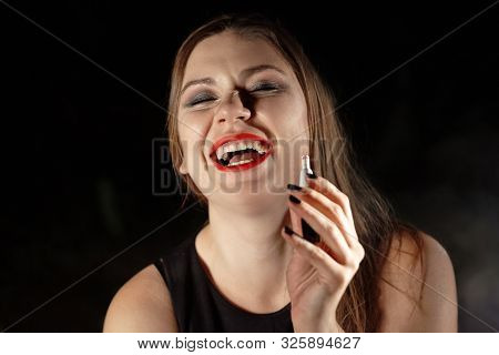 Young Brunette Woman Vaping E-cigarette With Smoke On Dark Background, Laughing, Drunk. Red Lipstick