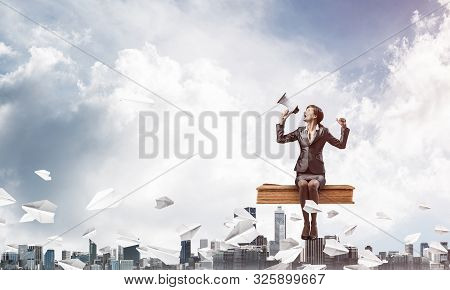 Young Woman With Megaphone Sitting On Big Book And Flying In Blue Sky. Pretty Businesswoman On Backg