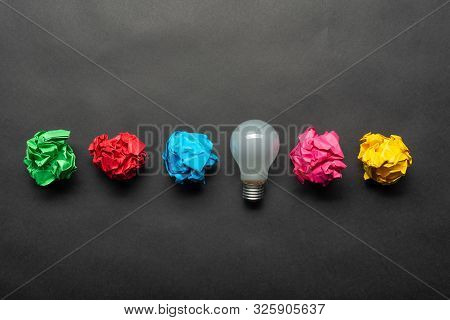Lightbulb And Crumpled Colorful Paper Balls On Black Background. Successful Solution Of Problem. Ide
