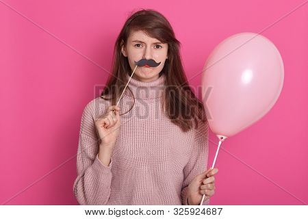 Stusio Shot Of Beautiful Young Girl Wearing Pink Sweater Standing And Holding Toy Mustache And Air B
