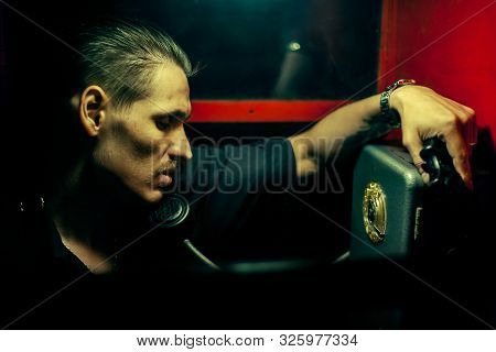 A Man Of Criminal Appearance In A Payphone Booth At Night. Talking On The Phone With A Revolver And