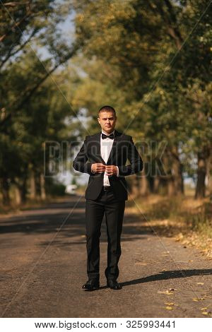 Young Man Walking In The Park. Handsome Groom In Black Suit