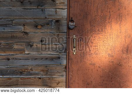An Old Brown Iron Door Locked With A Padlock. There Are Foci Of Rust. Part Of The Wooden Wall With T