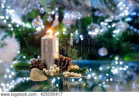 Silver Burning Candle With Christmas Decoration Of Fir Tree And Cones, In Front Of A Green Christmas