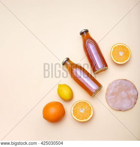 Two Bottles Of Kombucha Tea, Scoby And Citrus Fruits For Additional Flavors On Yellow Pastel Backgro