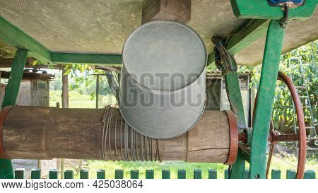An Old Water Well With A Bucket In The Garden, A Metal Handle For Lifting Water From The Ground. Vil