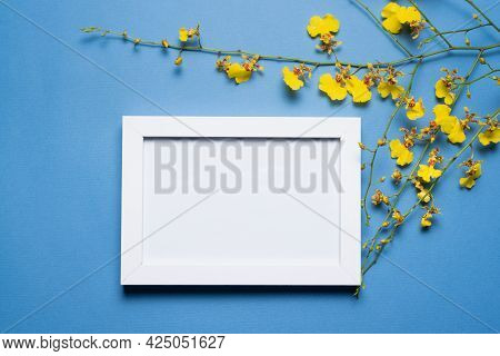Blank Empty Picture Frame With Copy Space And Oncidium Orchid Flowers Branch On The Blue Flat Lay Ba