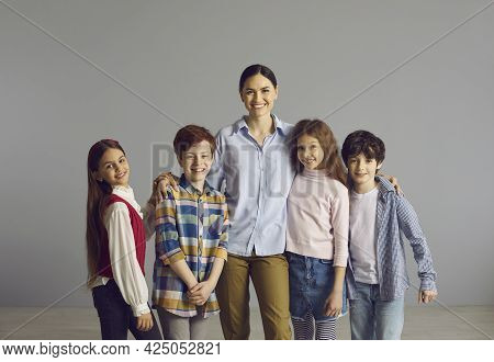 Happy Smiling Schoolteacher Posing With Her Pupils Over Studio Grey Background