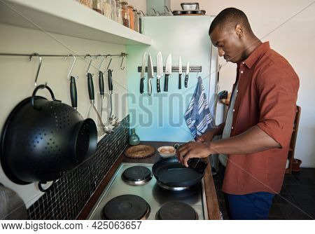 Young African Man Pouring Cooking Oil Into A Frypan