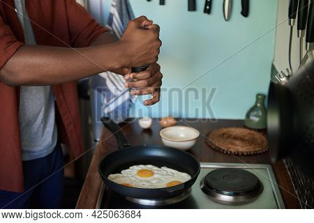 African Man Adding Salt To Some Eggs In A Frypan