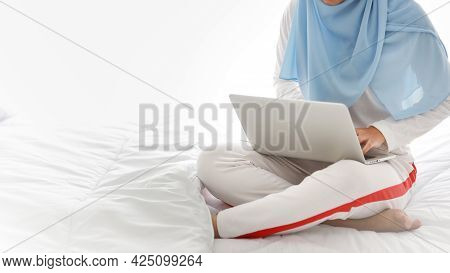 Young Asian Muslim Woman Hands Use Laptop Sitting On Bed In Bedroom. Beauty Girl In White Sleepwear 